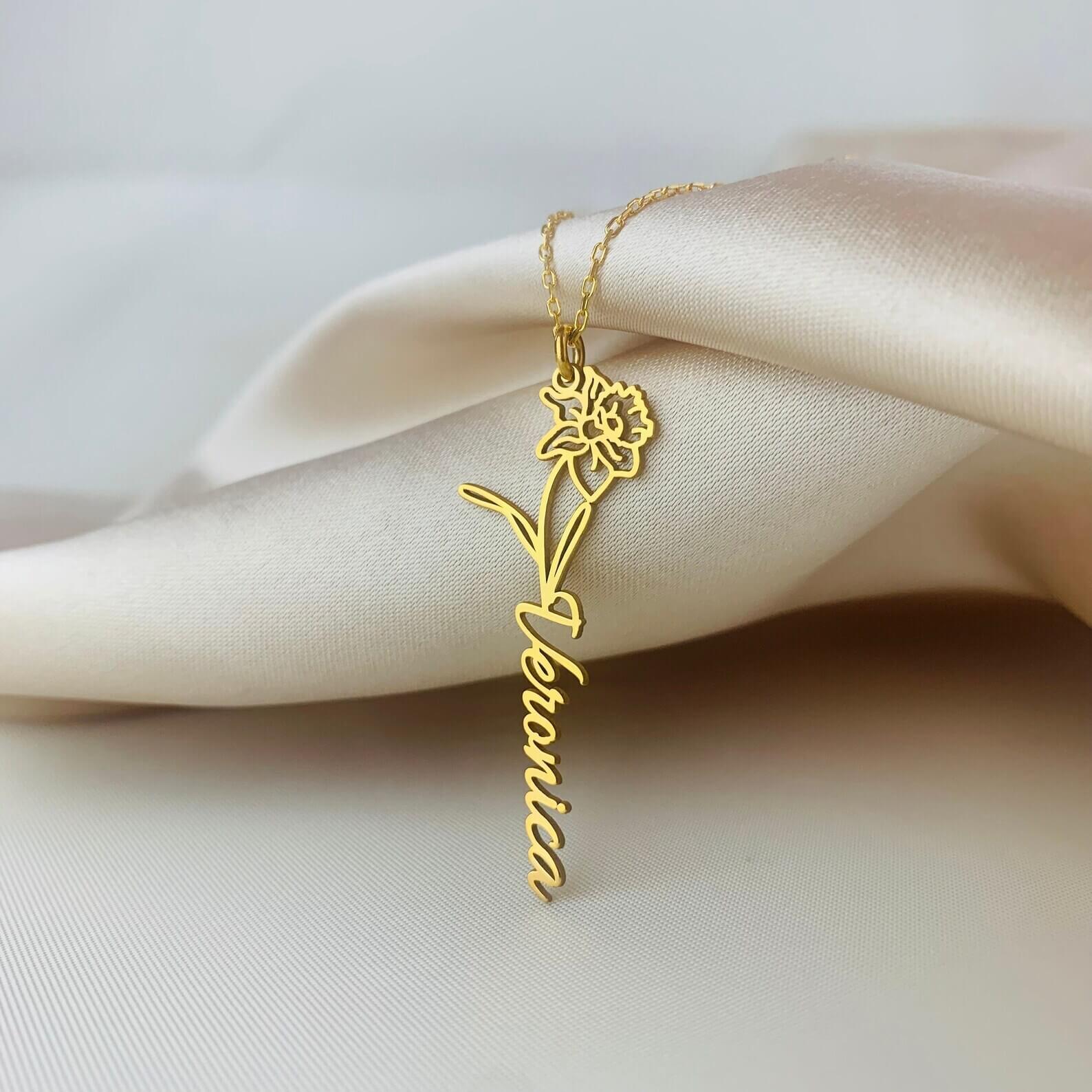 Gold necklace with a floral design and 'Veronica' engraving on a beige fabric background