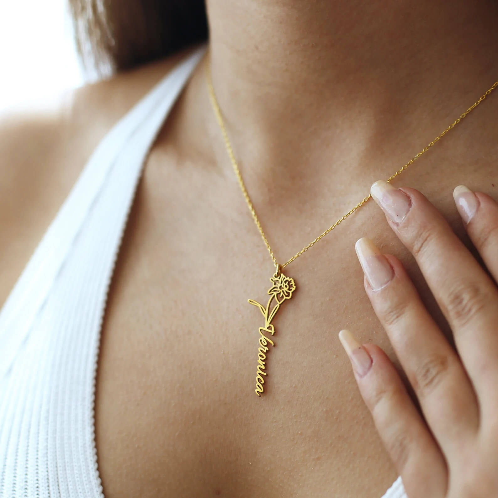 Gold necklace with a pendant on a person wearing a white top.
