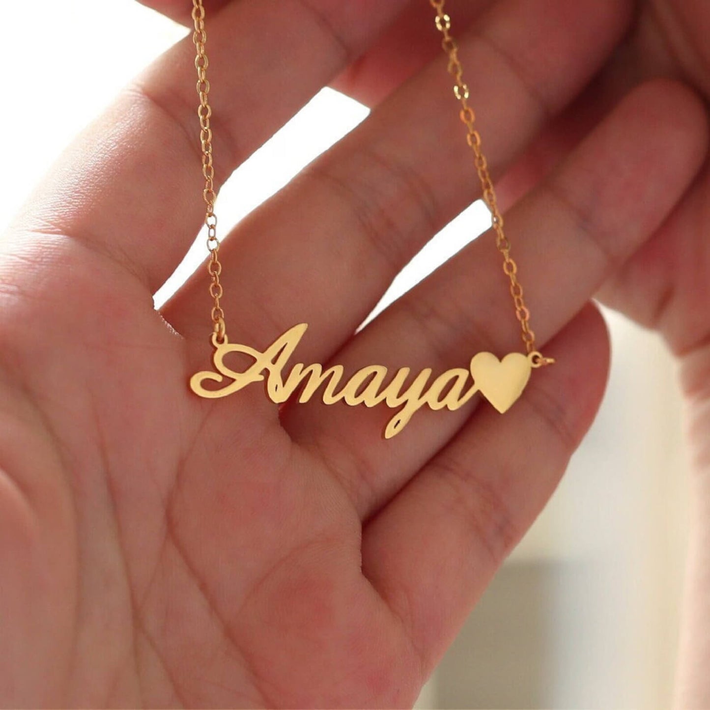 Gold necklace with 'Amaya' pendant held in a hand