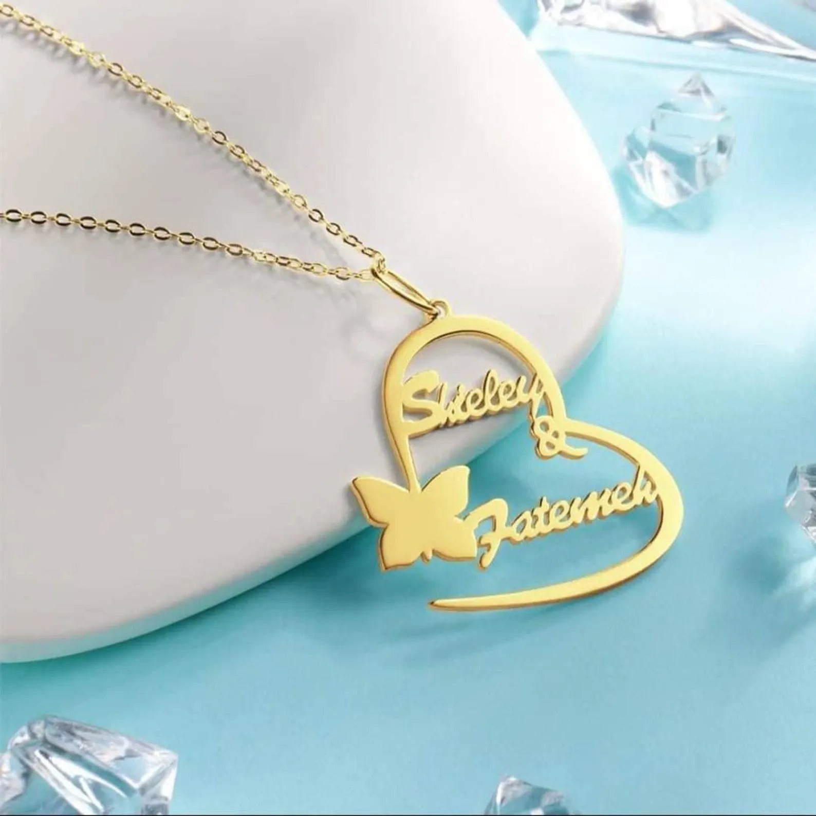 Gold heart-shaped necklace with butterfly pendant on a light blue background